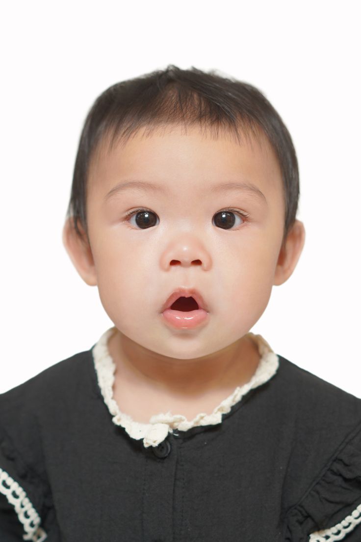Surprised Asian baby girl with open mouth wearing a black dress, isolated on white background.
