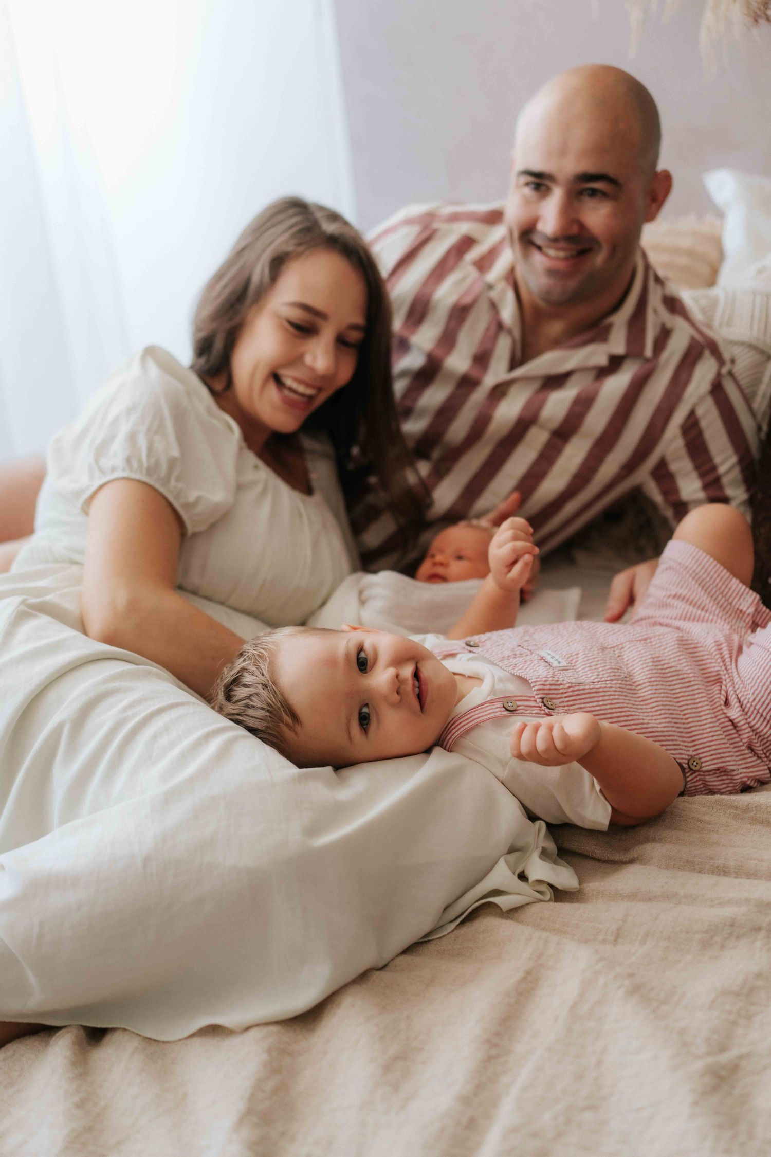 A family sharing joyful moments together while relaxing on a cozy bed with white bedding.