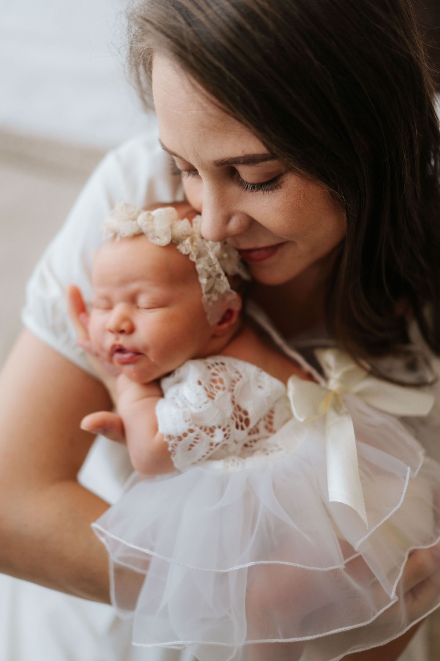 A tender moment between parent and baby in white christening dress captured in soft natural light.在柔和的自然光下，父母與身穿白色洗禮服的嬰兒之間溫馨的一刻被捕捉了下來。