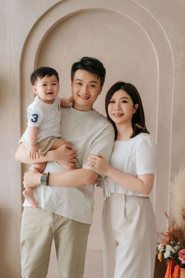 Asian family portrait with father holding toddler boy and mother posing together under arch backdrop.