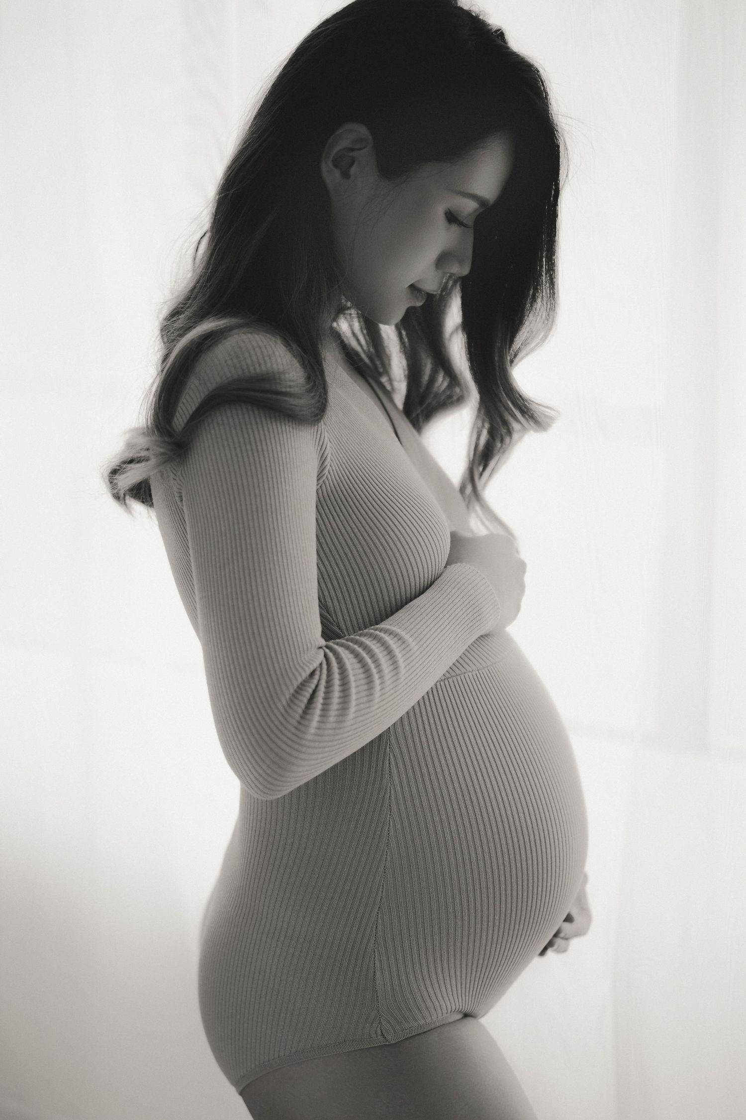 A series of black and white maternity photos showing a pregnant woman in a white sweater posing against a light background.