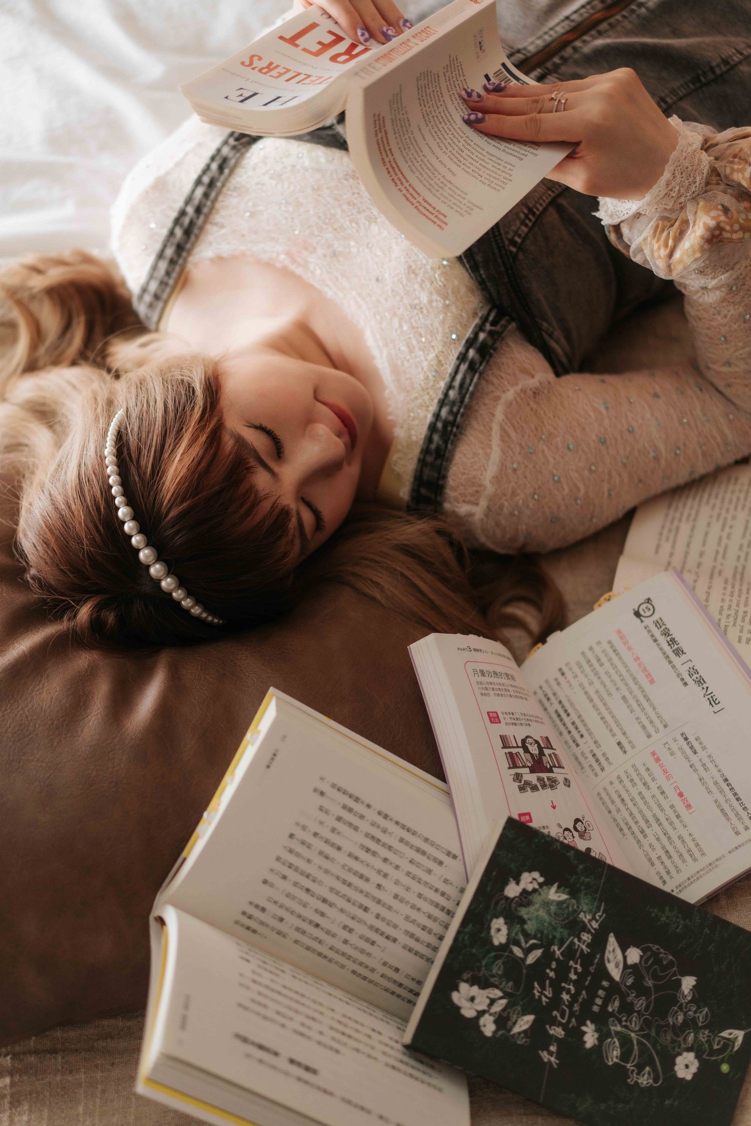 Person lying down surrounded by open books while reading in cozy setting with natural light.一個人躺在被打開的書包圍的舒適環境中閱讀，周圍是自然光。