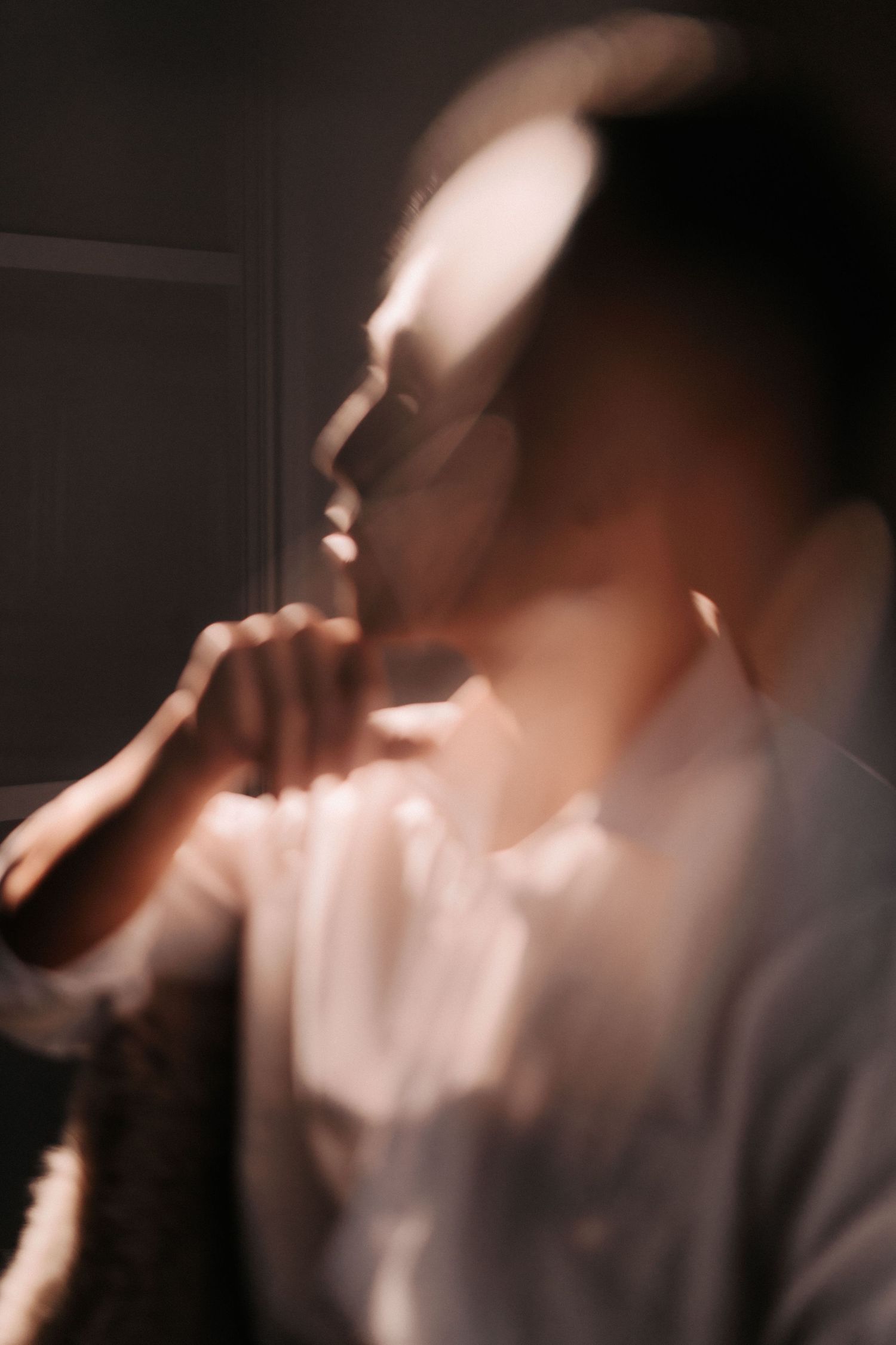 Blurred artistic portrait of a person in white shirt with glasses, contemplating in dramatic moody lighting.