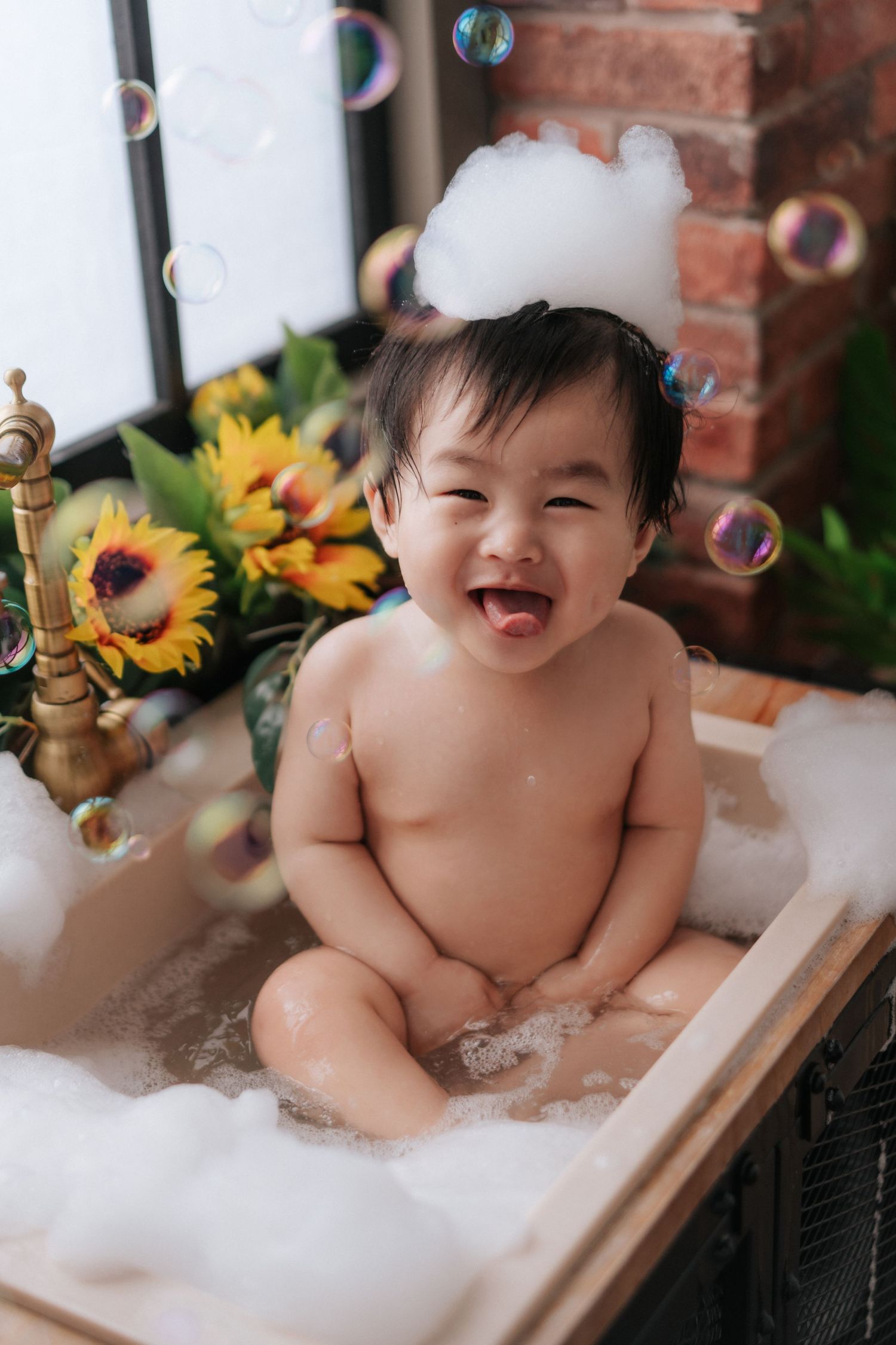 Smiling baby sitting in a bubble bath with foam on head, surrounded by colorful bubbles and sunflowers.一個微笑的嬰兒坐在泡泡浴中，頭上蓋著泡沫，周圍環繞著五彩繽紛的泡泡和向日葵