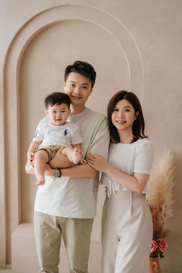 Young Asian family portrait with father holding baby boy and mother beside them in neutral tones.