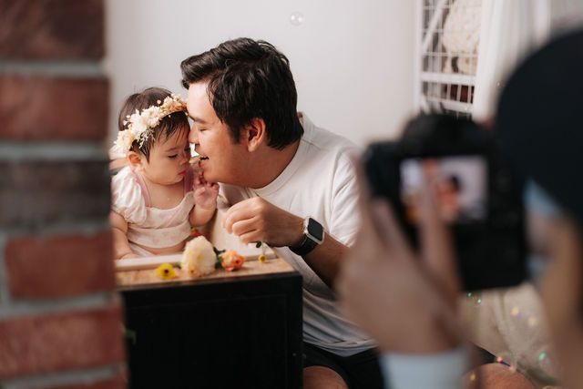 A father shares a tender moment with his flower crown daughter at a birthday cake smash session.