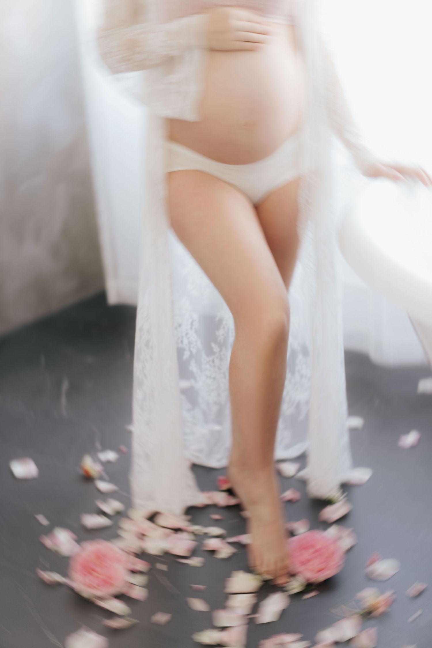 Delicate lace wedding dress hem swishes over scattered pink and white rose petals on a dark floor精緻的蕾絲婚紗裙擺在散落在深色地板上的粉紅色和白色玫瑰花瓣上輕輕搖曳。