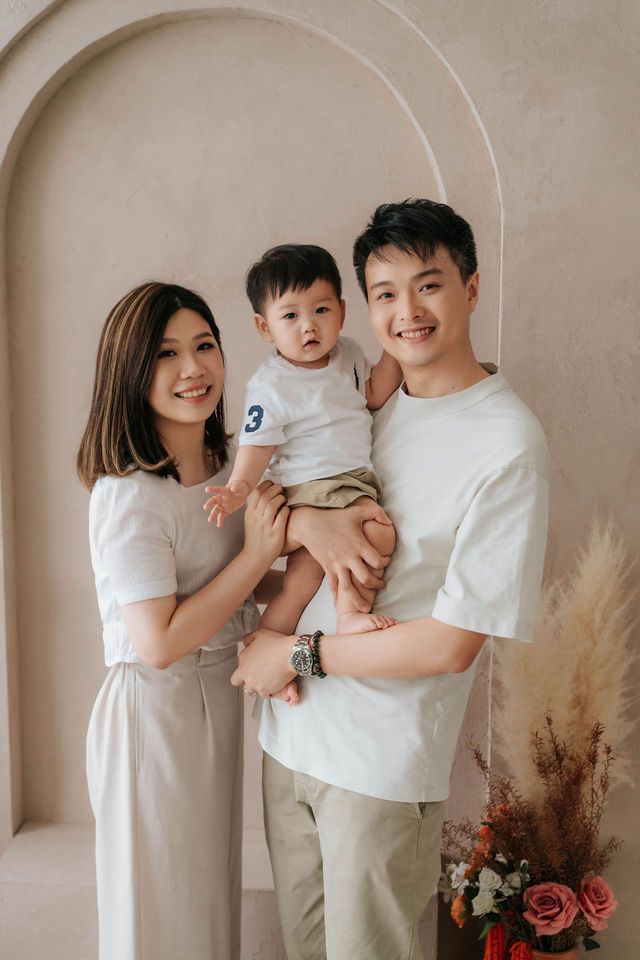 Happy Asian family photo with mother and father holding toddler son in a bright studio setting.