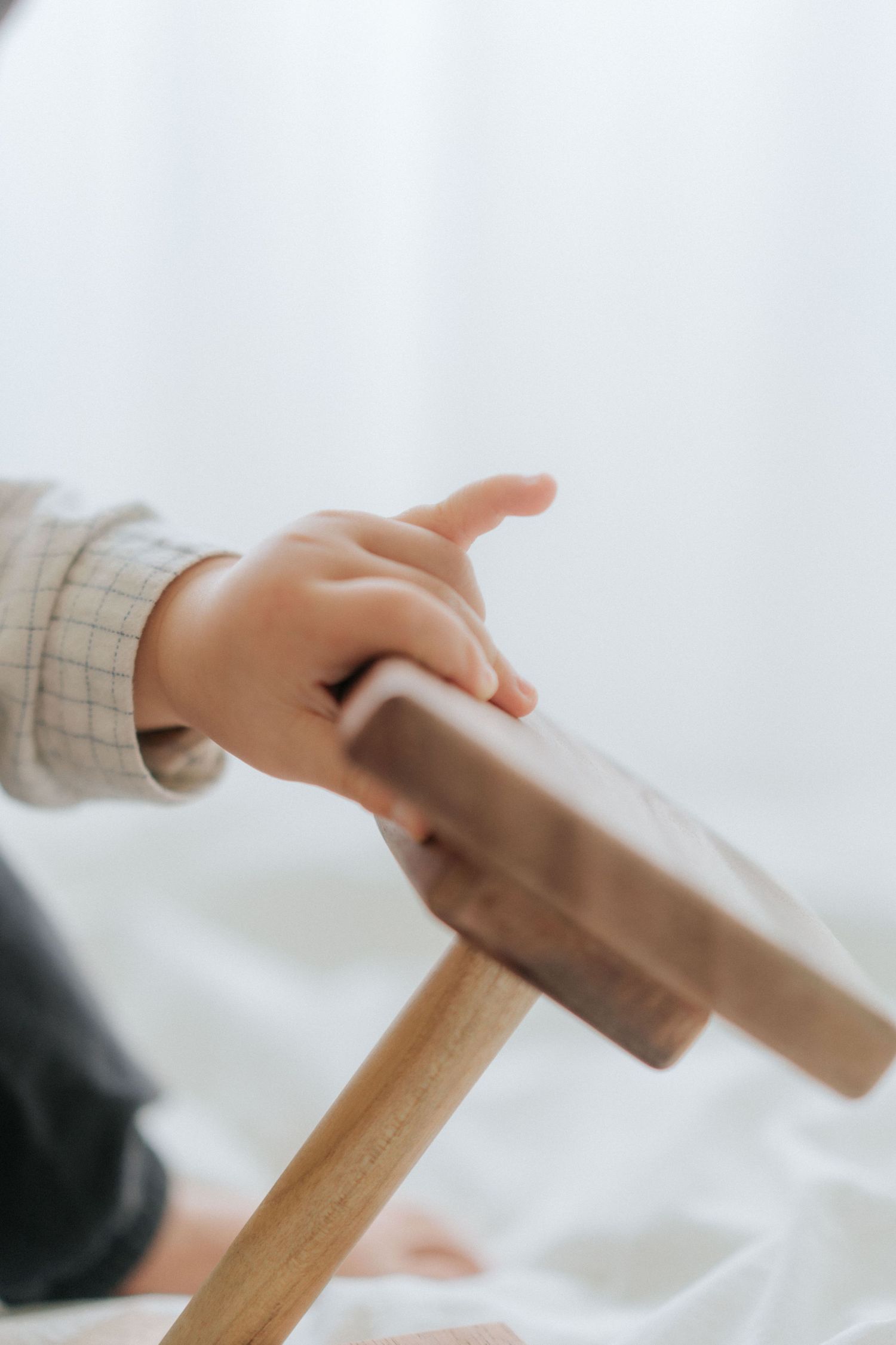Close-up of a toddler's hand gripping a wooden furniture rail, wearing a plaid shirt.
