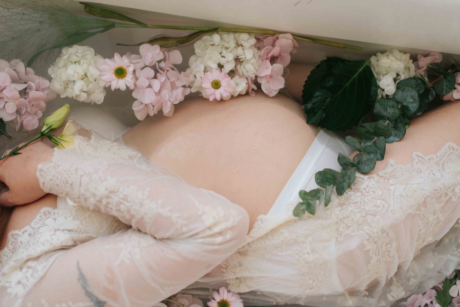 Delicate white lace wedding dresses hang in a row with floral embellishments and soft pink accents.