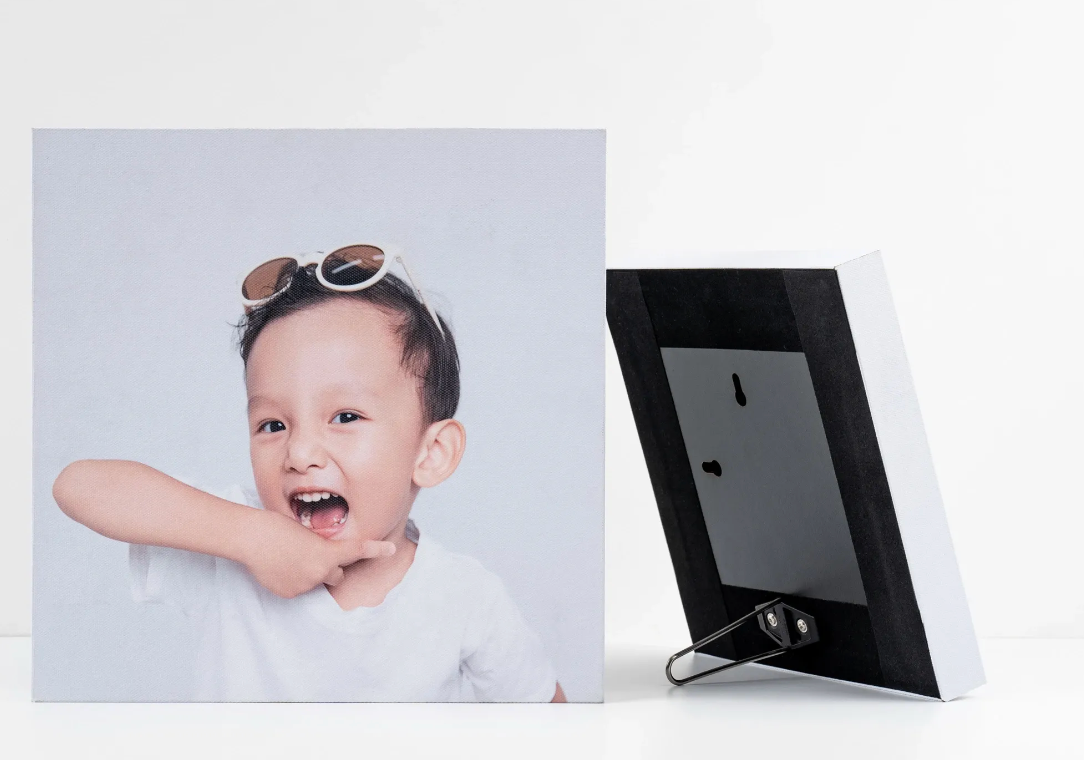 A smiling young boy with sunglasses on his head displayed in a square photo print beside a small digital picture frame.