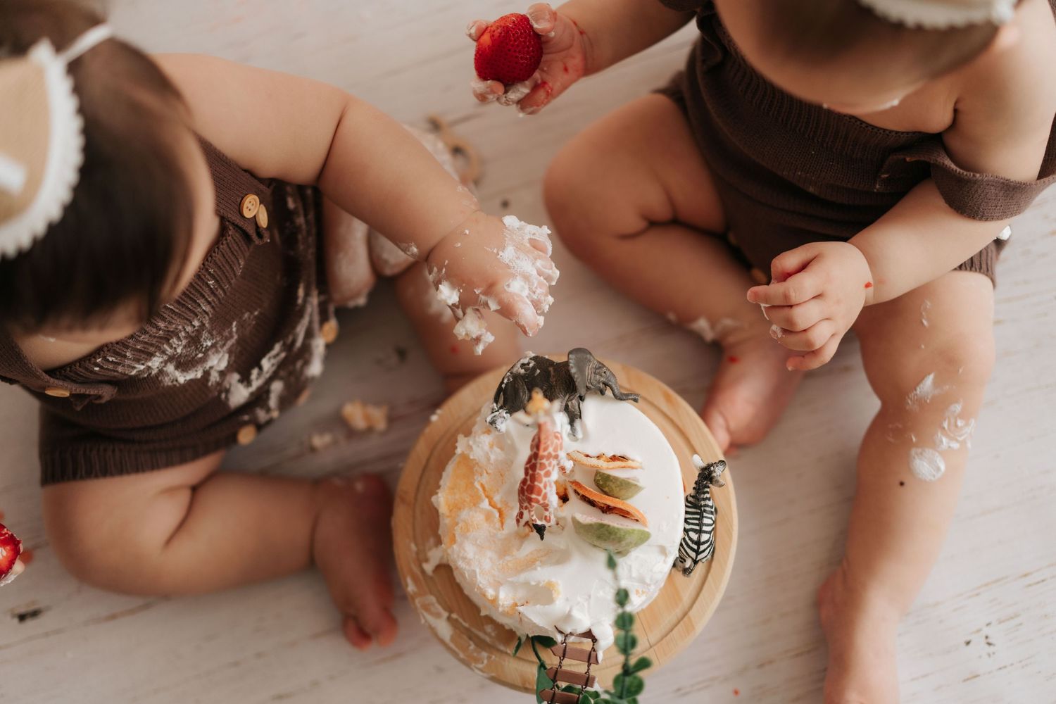 Baby hands reach for a cake smash birthday celebration with frosting and decorations on a white wooden floor.嬰兒的小手伸向鋪著糖霜和裝飾品的白色木地板，參加生日蛋糕砸臉慶