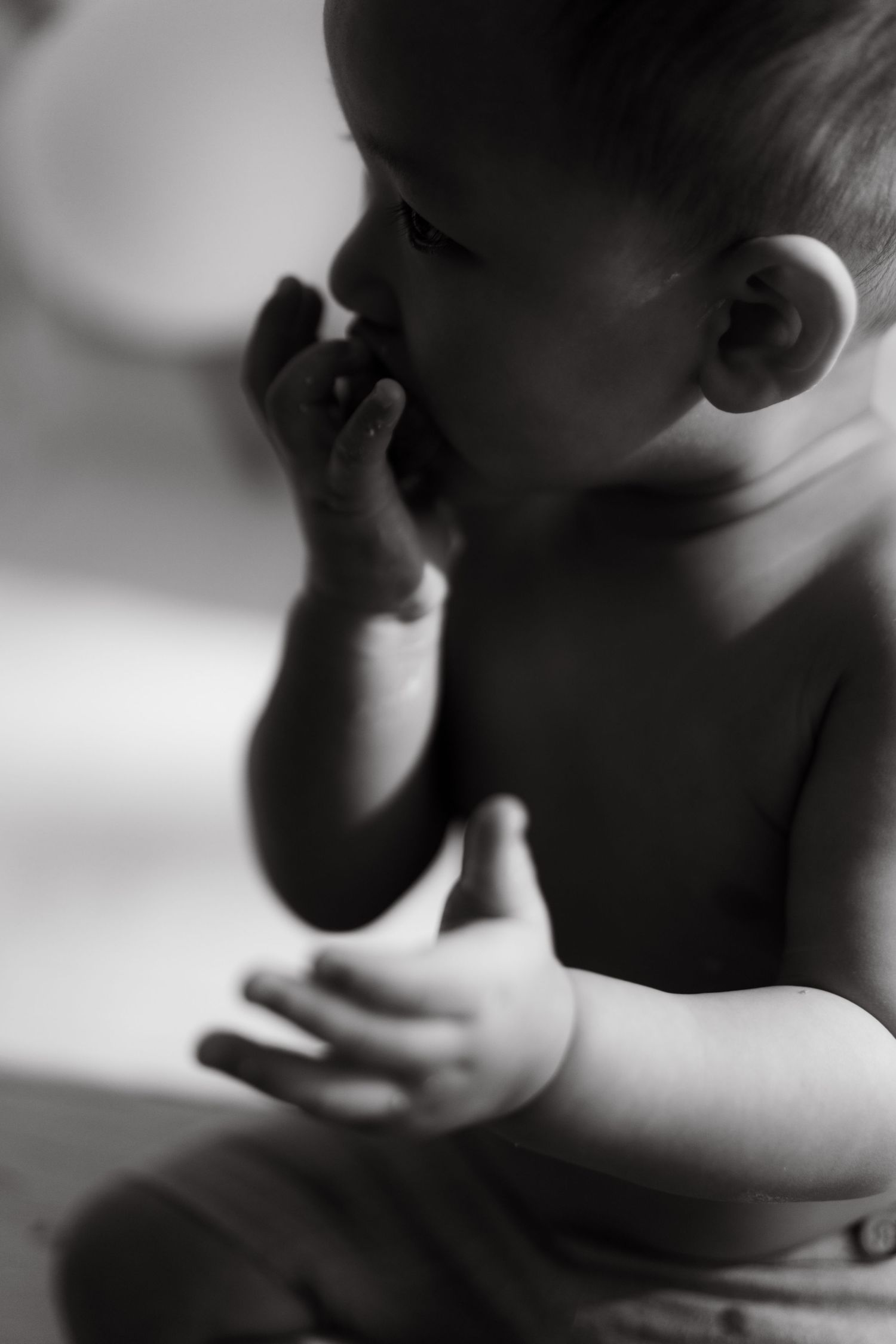 Black and white artistic portrait of a baby's hands and profile in soft natural lighting.黑白藝術肖像，柔和的自然光線下，嬰兒的小手和側臉。