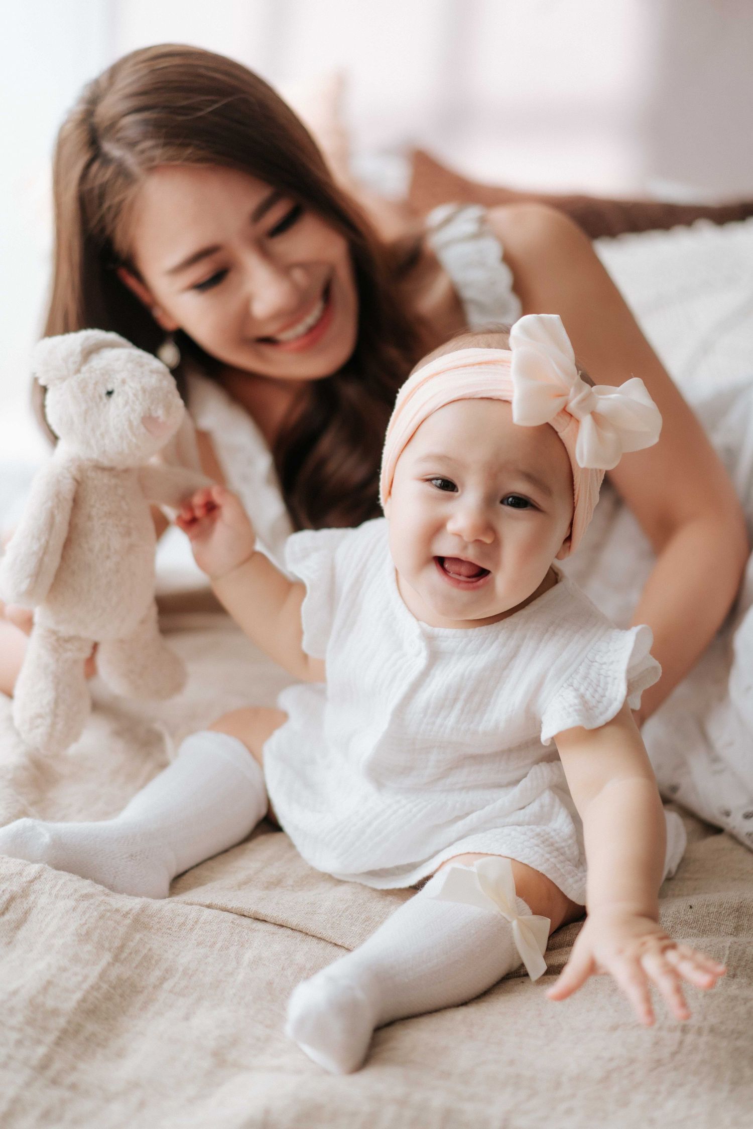 A heartwarming series of photos showing a baby in white clothing playing and laughing on a light-colored bed.一組溫馨的照片，照片中一個身穿白色衣服的嬰兒在淺色床上玩耍嬉戲