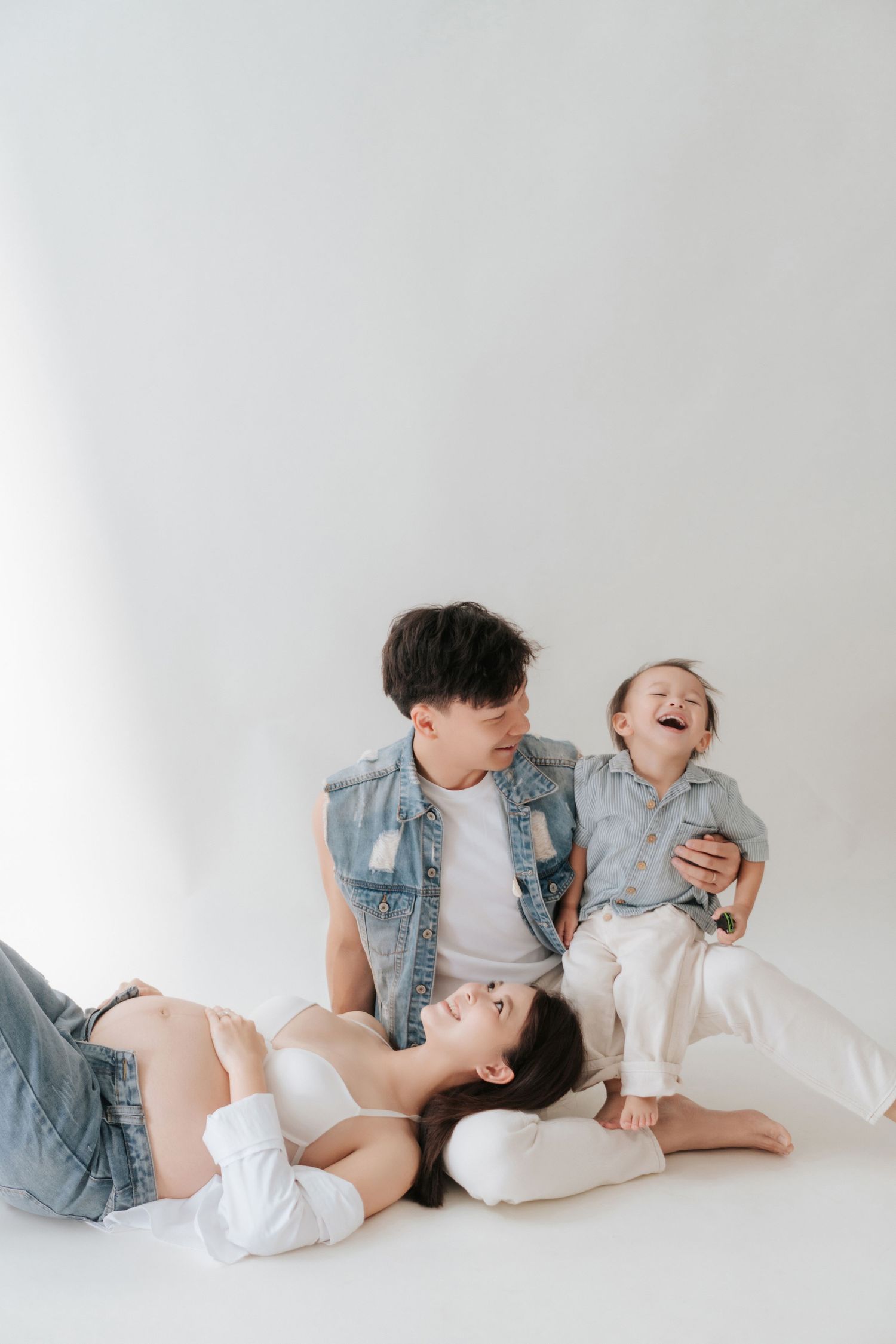 Family members lying on white floor wearing denim and white clothing share joyful laughter together.