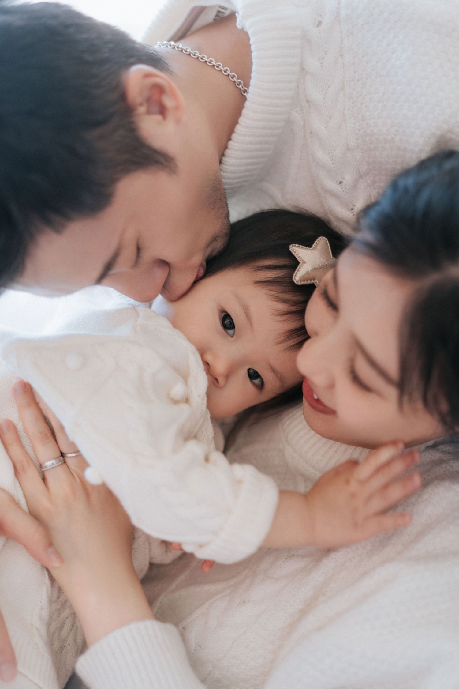 A series of tender family moments showing a parent and child cuddling together on white bedding.一系列溫馨的家庭瞬間，展現了父母和孩子在白色床單上依偎在一起的畫面。