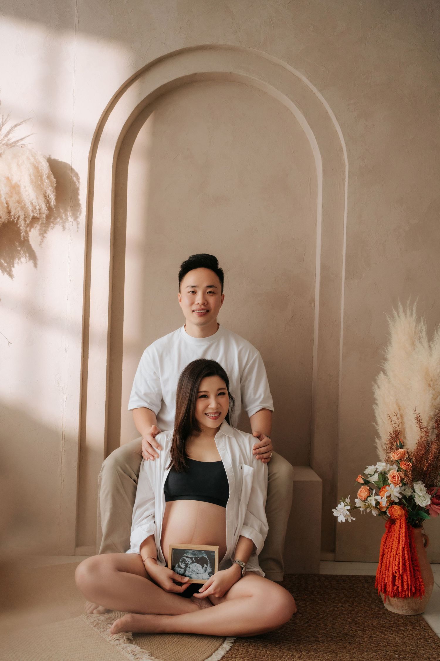 A series of maternity photos showing a pregnant person in a white shirt against a neutral backdrop with arched windows.