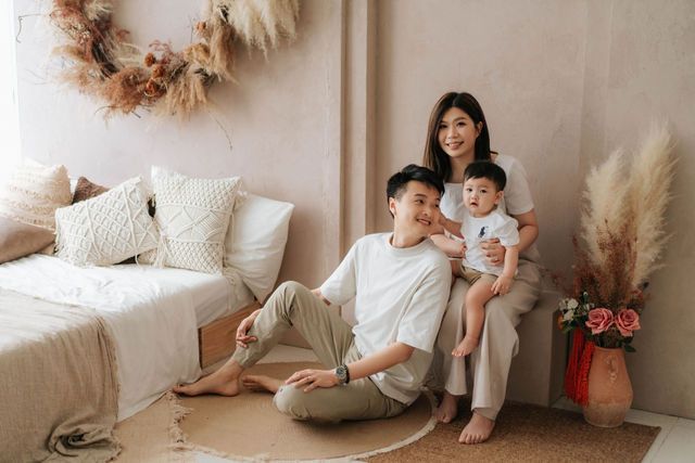 Happy Asian family with parents and baby posing together in a cozy boho-styled living room with neutral tones.