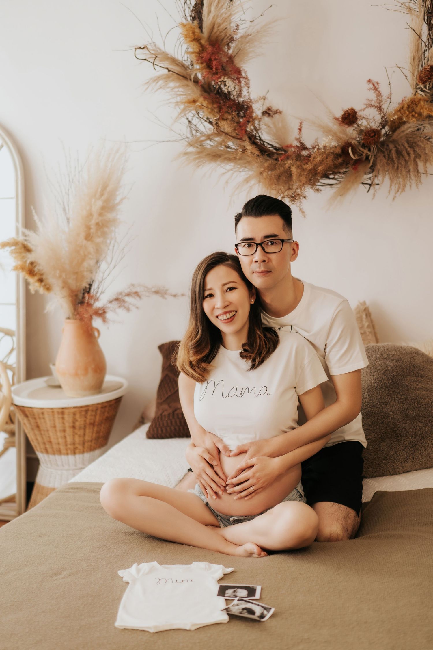 Warm toned maternity photo series showing intimate moments on bed with neutral decor and pampas grass in background.