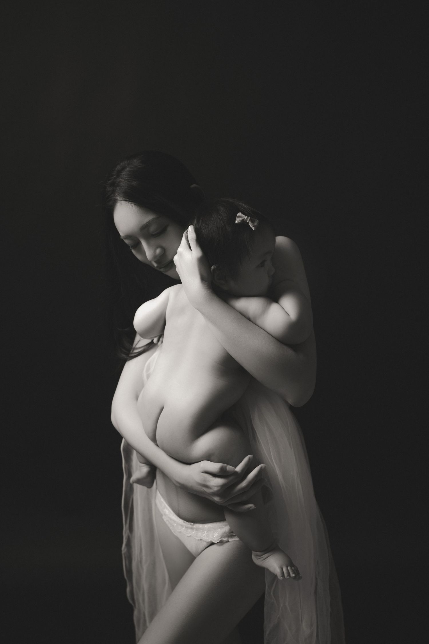 Black and white artistic nude photograph showing a delicate pose with flowing fabric against a dark background.黑白藝術裸體照片，展現了柔美的姿態，飄逸的衣料在深色背景下