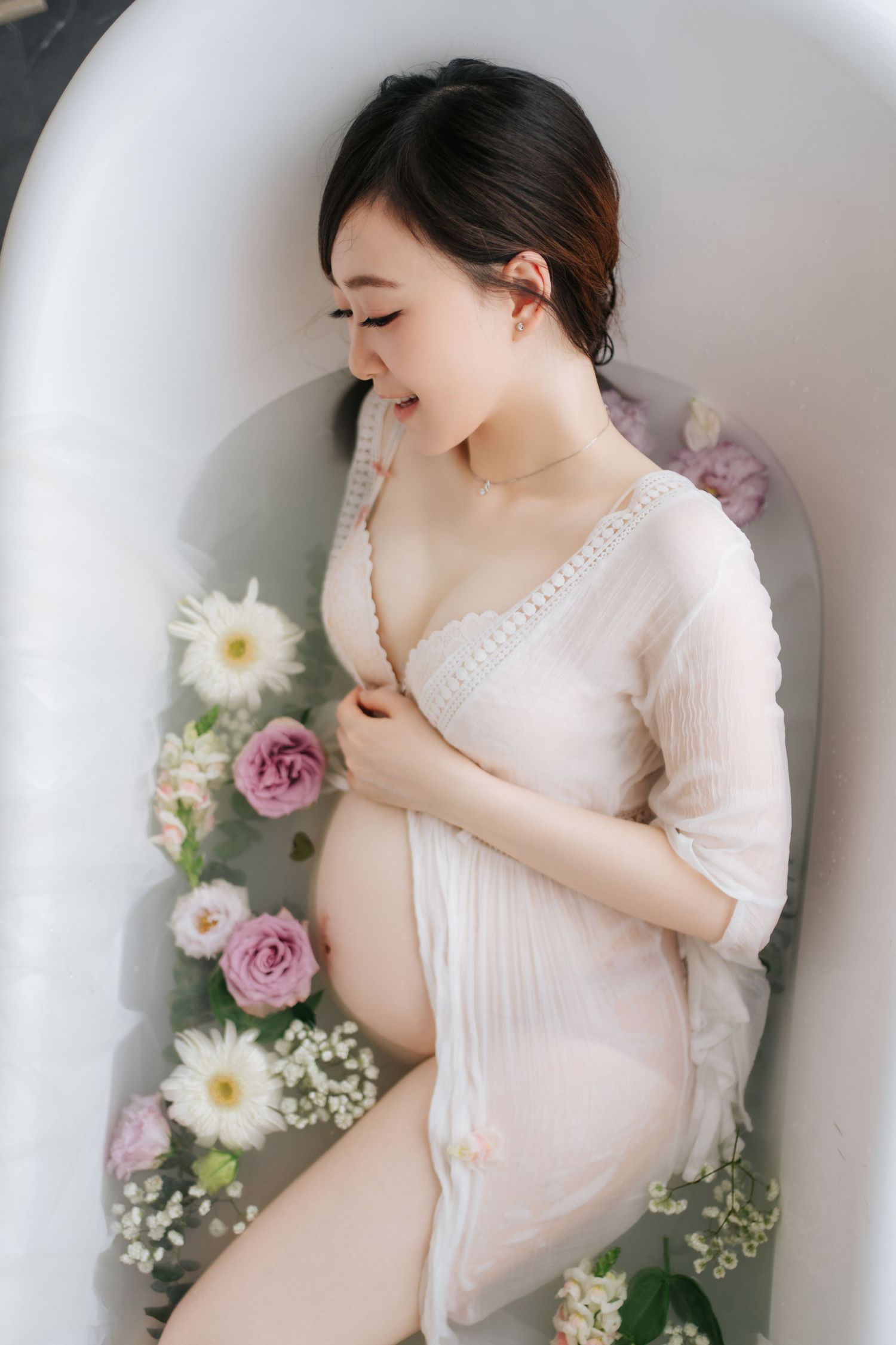 Elegant maternity photoshoot featuring soft pink dress and delicate purple and white floral arrangements against white wall優雅的孕婦寫真，身穿柔粉色連身裙
