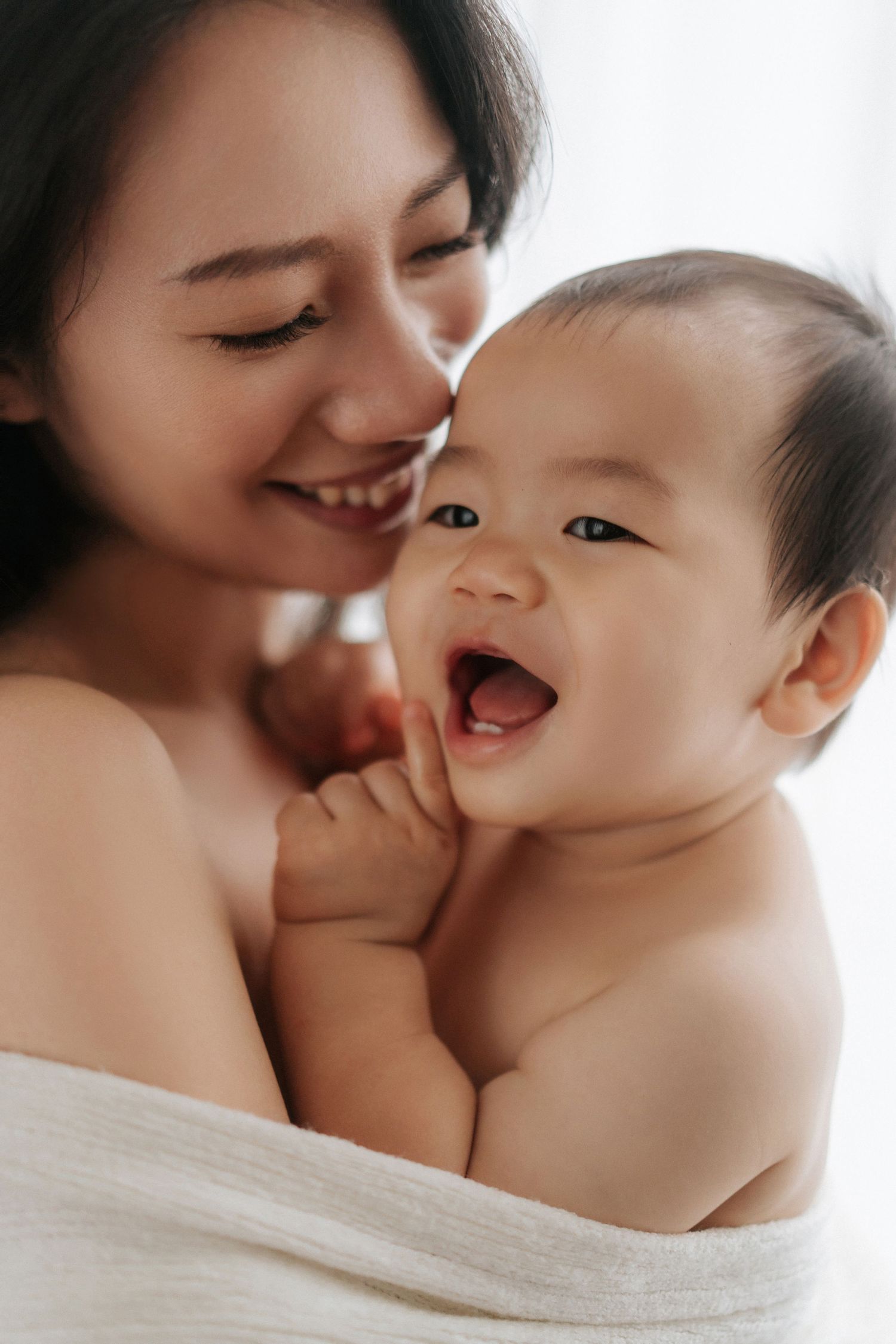 A tender moment between parent and baby as they share joyful laughter while wrapped in soft white fabric.父母與嬰兒裹在柔軟的白色布料中，歡聲笑語，溫馨的一刻。
