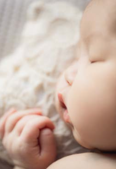 Close-up view of a sleeping baby's face nestled in soft white bedding.特寫鏡頭展現了熟睡的嬰兒臉龐，它依偎在柔軟的白色床單中。