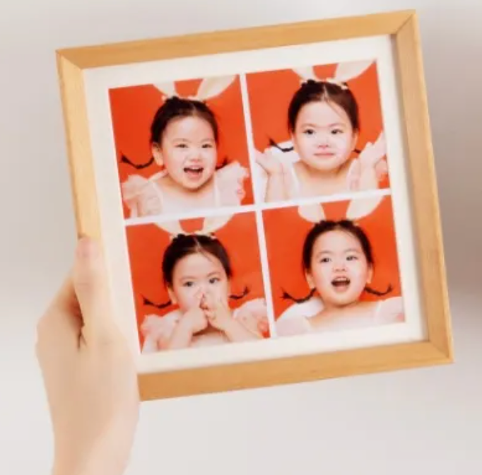 A framed photo collage of four cute toddler portraits on an orange background, held by a hand.