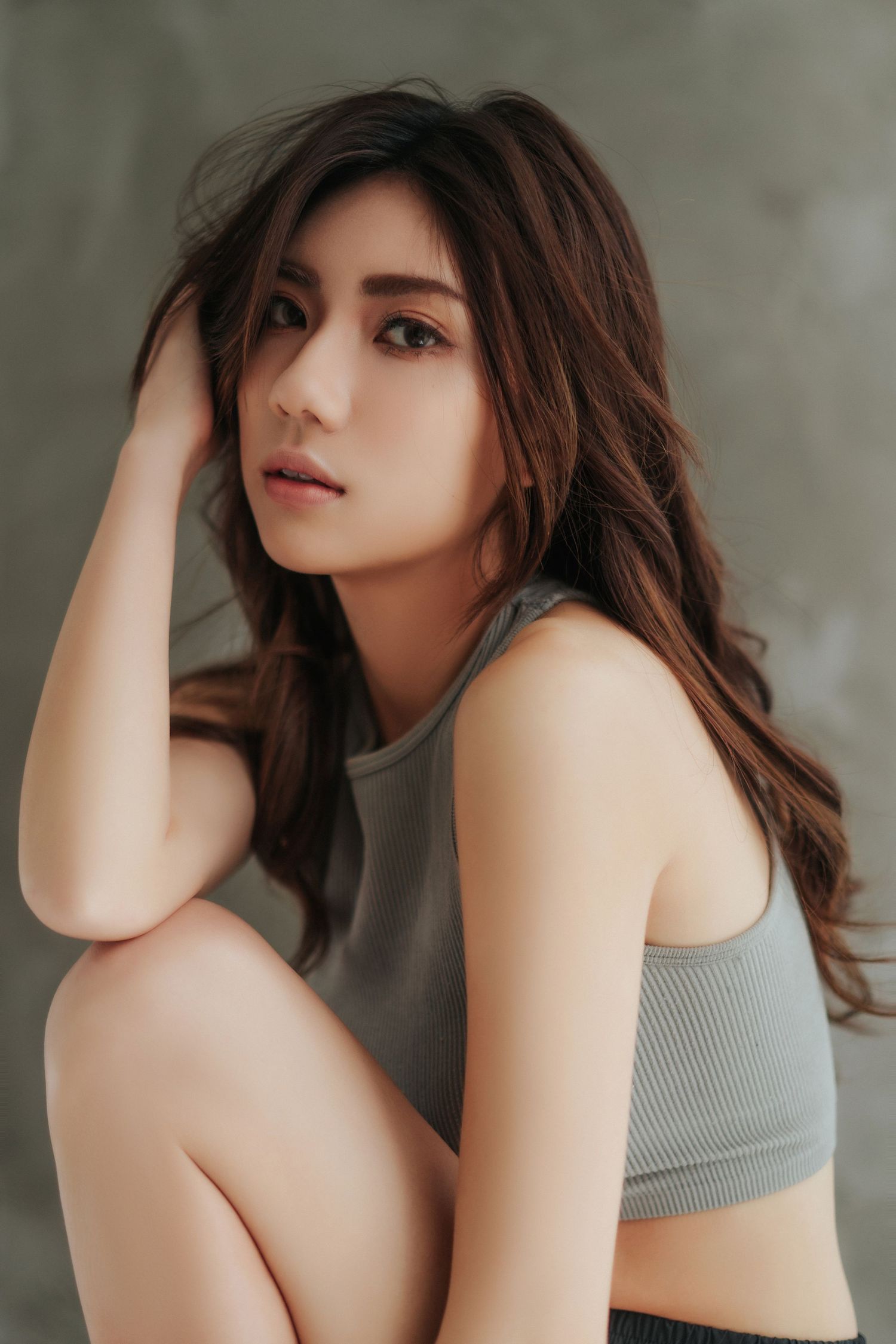 A woman in a gray sports bra poses sensually against a neutral background in a fashion photography series.在一組時尚攝影作品中，一位身穿灰色運動胸罩的女子在素雅的背景下