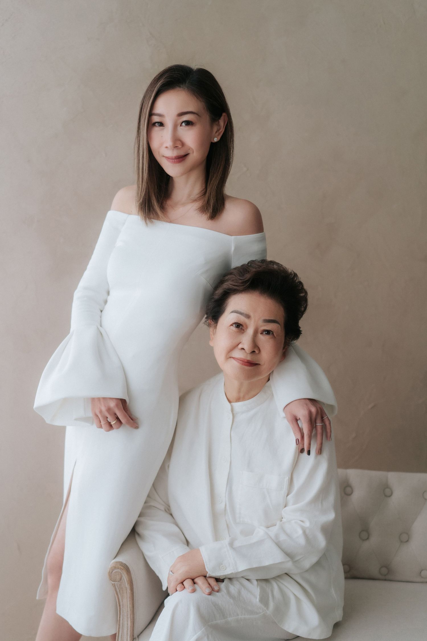 Two people in white outfits pose together against a neutral wall in a minimalist studio portrait session.兩名身穿白色服裝的人在極簡風格的影棚人像拍攝中，倚靠在一面中性色調的牆