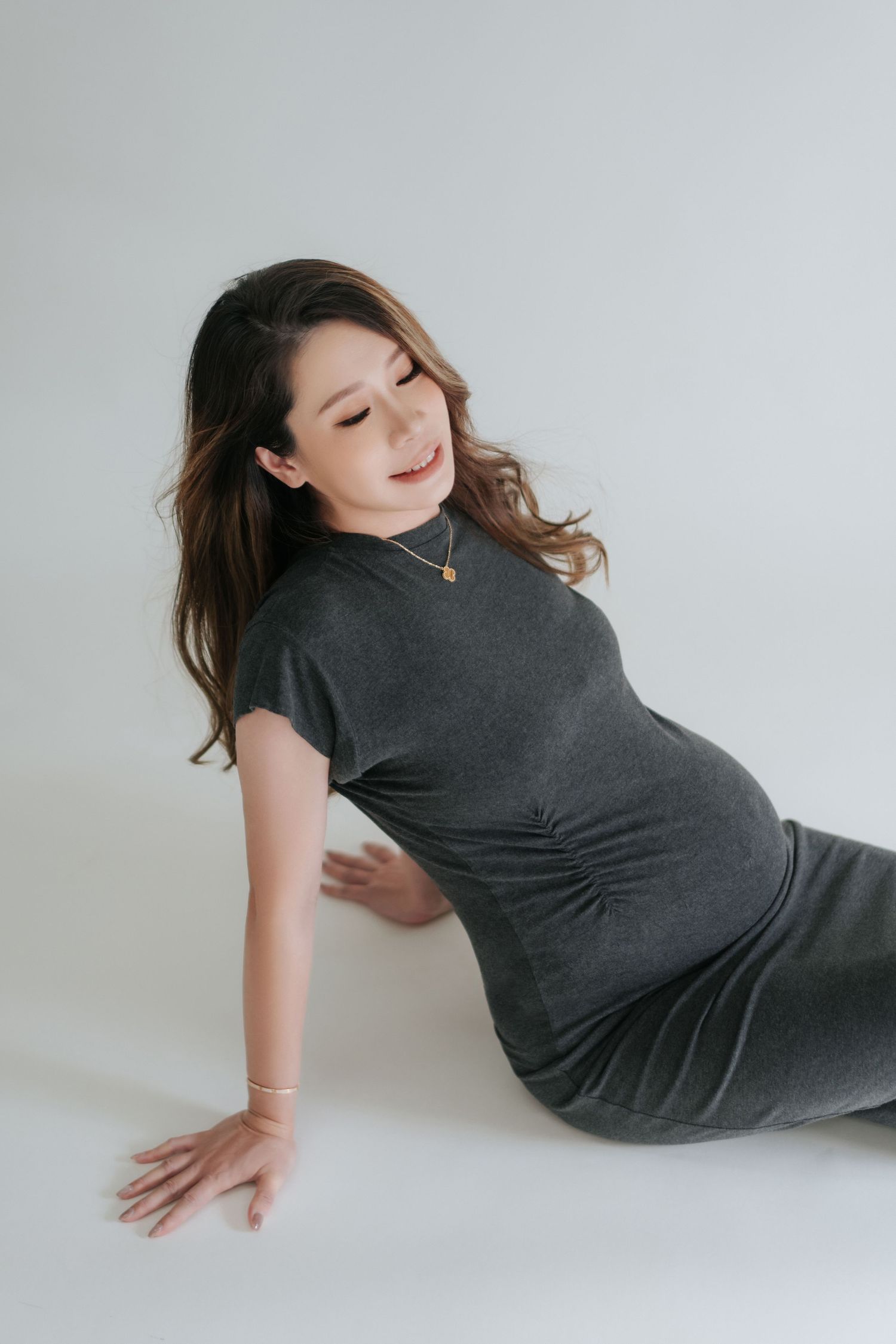 A sequence of artistic maternity portraits showing a person in a dark gray dress posing gracefully against a white backdrop.