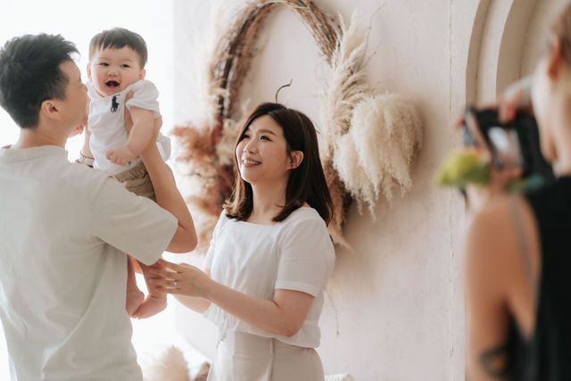 Happy Asian family with parents smiling at laughing baby during a bright indoor photo session.