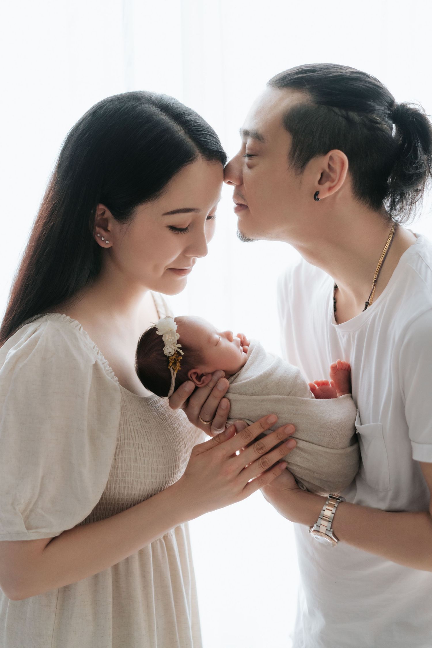 Young Asian couple tenderly holding their newborn baby together, touching foreheads in an intimate family portrait一對年輕的亞洲夫婦溫柔地抱著他們剛出生的寶寶，額頭相