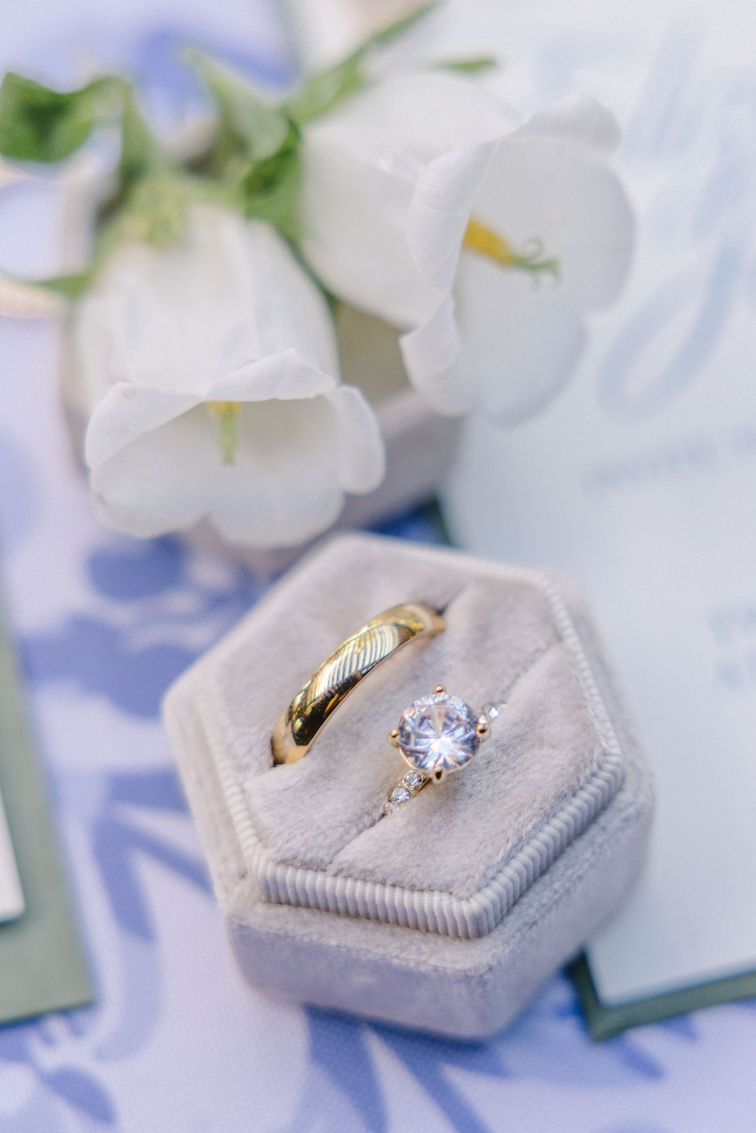 Wedding rings displayed in a light gray velvet ring box with white flowers.
