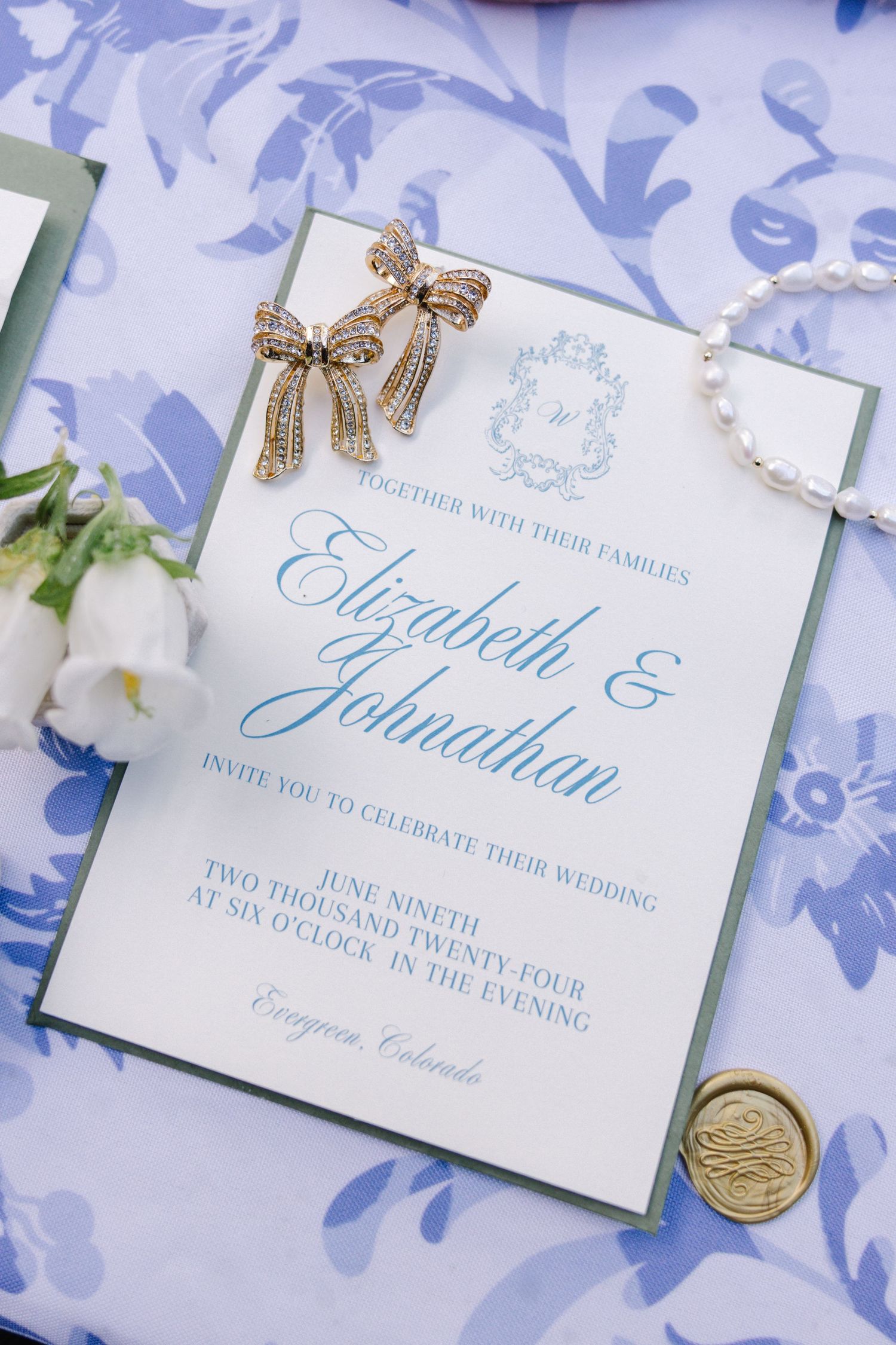 Wedding invitation with blue calligraphy and gold wax seal on floral background.
