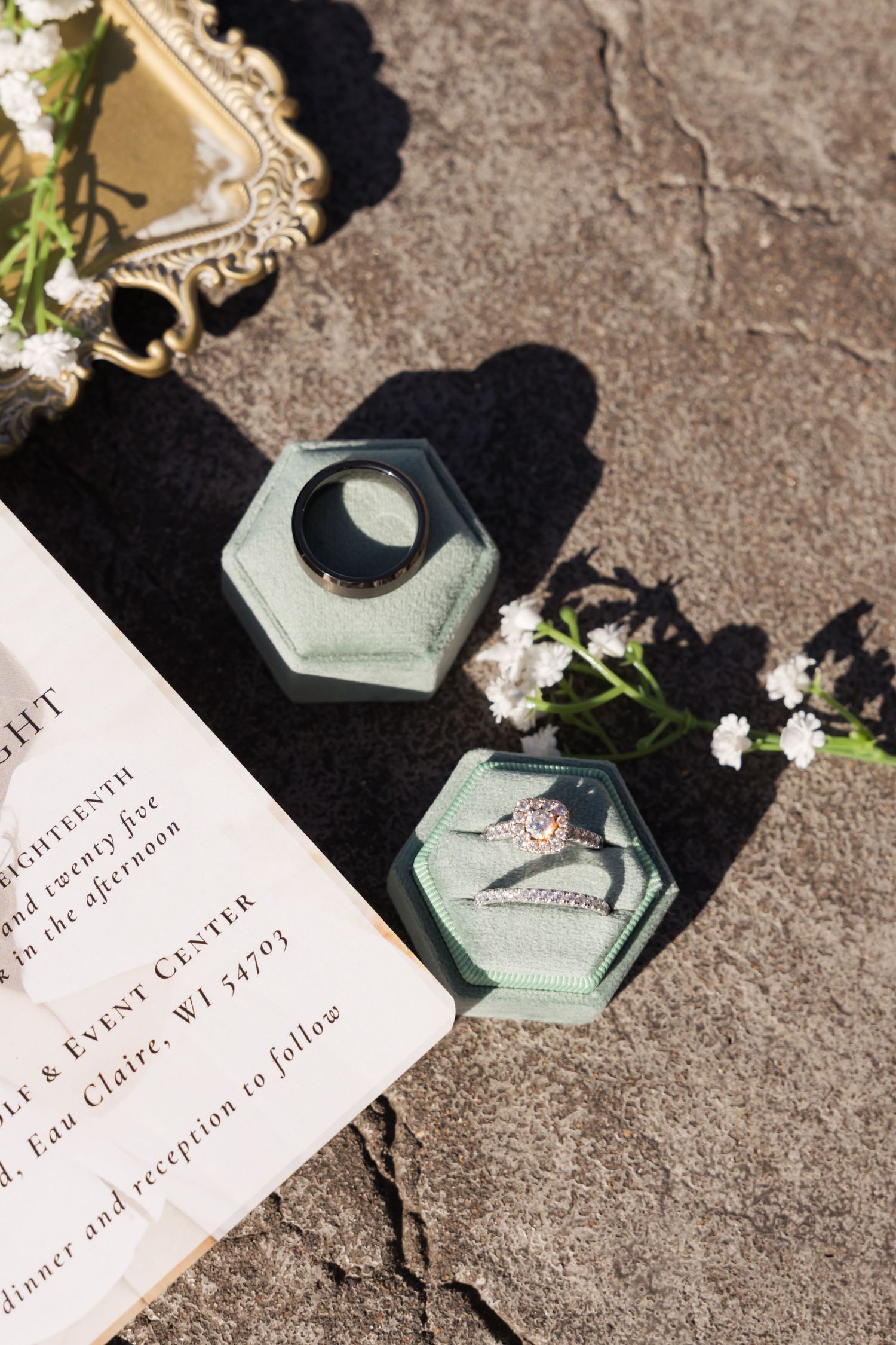 Wedding rings casting shadows on textured stone surface with elegant invitation details.