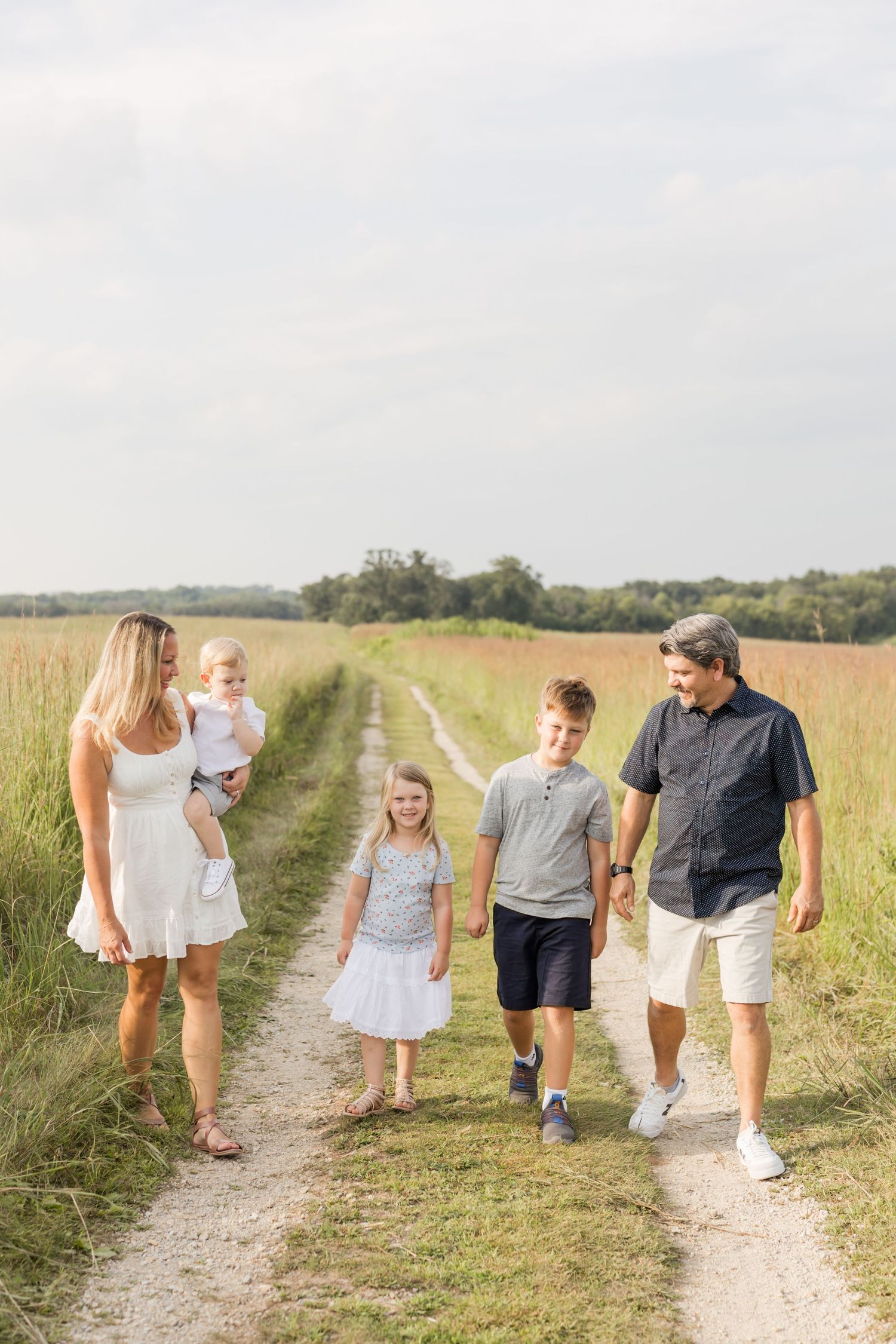 Family walking together on dirt path through tall prairie grass.