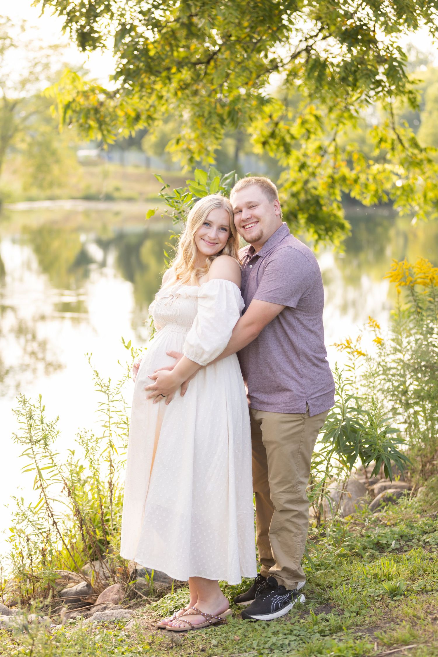 Expecting couple poses together by lake during sunset maternity photo session.