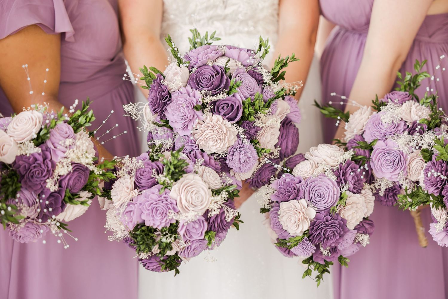 Purple and white floral bouquets arranged in a row with matching bridesmaid dresses.