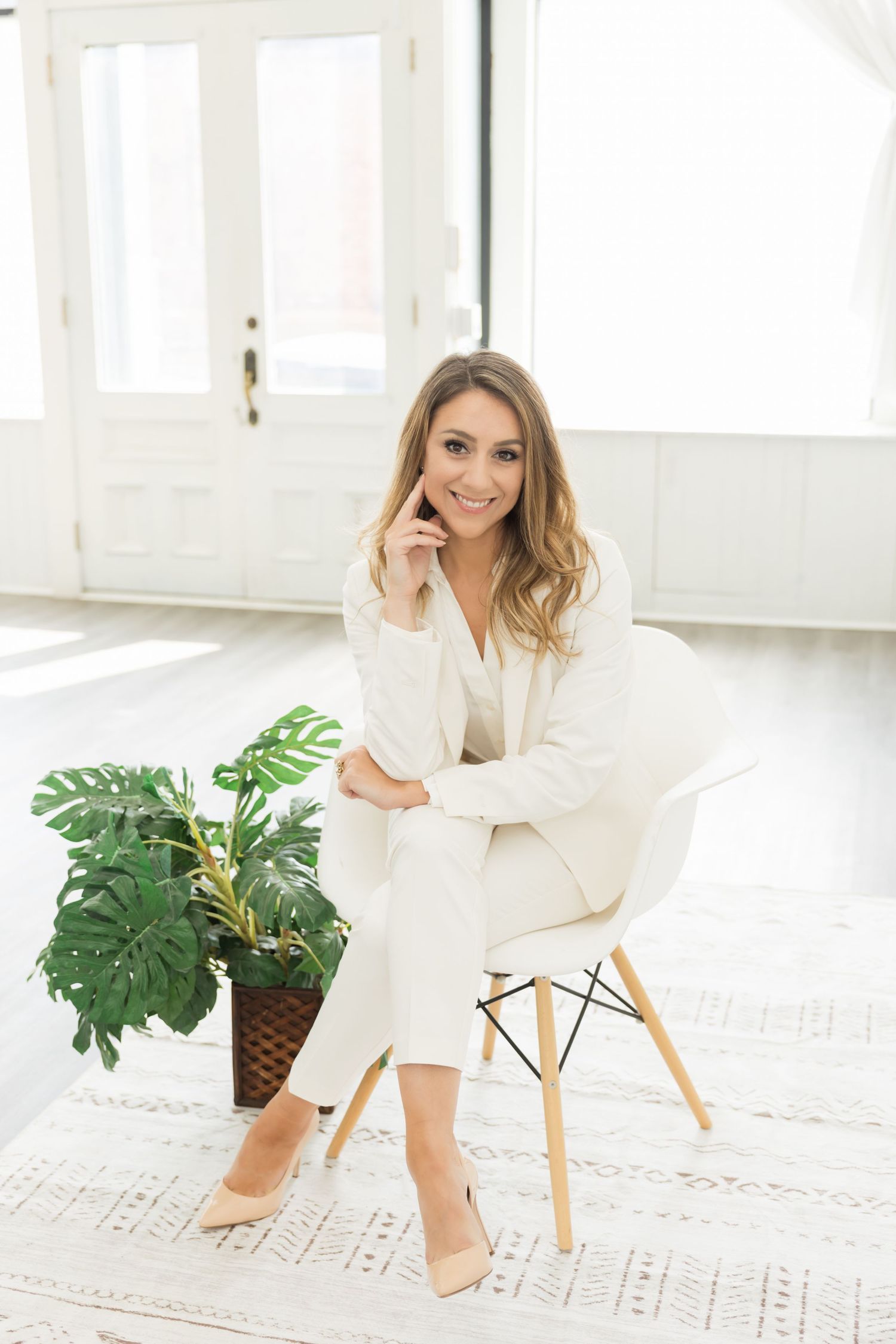 Person in white loungewear sits on modern chair in bright minimalist room with monstera plant.