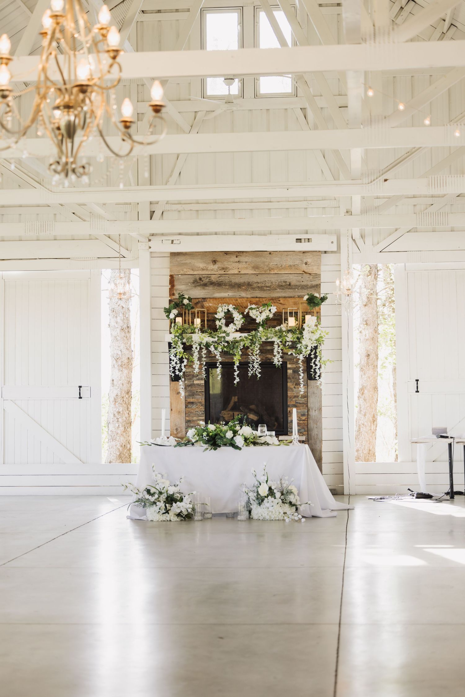 Bright white barn wedding venue with crystal chandeliers and natural light streaming through windows.