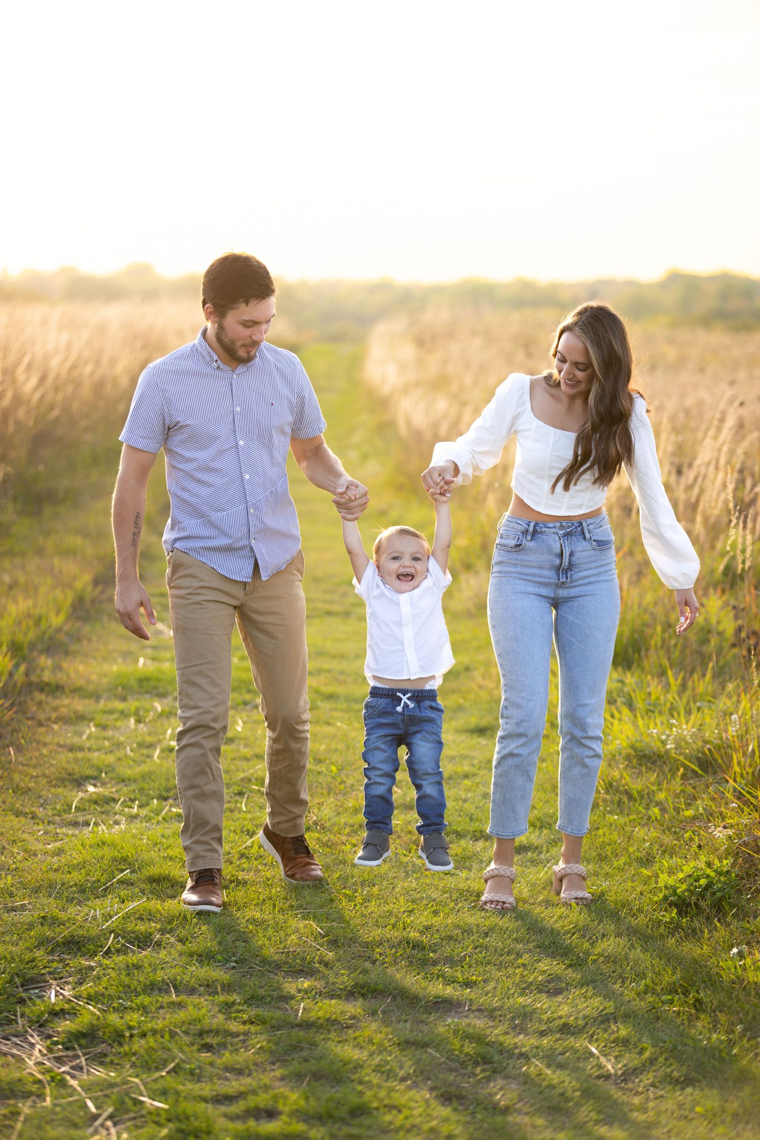 Family holding hands while walking through a sunlit meadow during golden hour.
