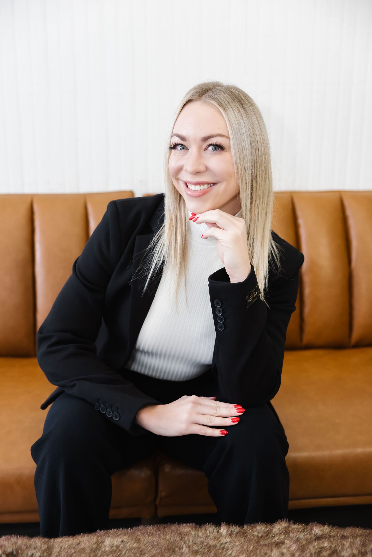 A person in a black blazer and gray top sits casually on a brown leather couch in a series of candid poses.