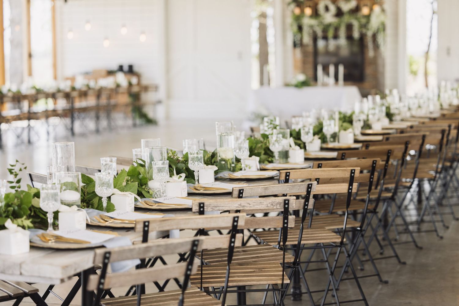 Long rows of elegantly set wedding reception tables with wooden chairs and white linens.