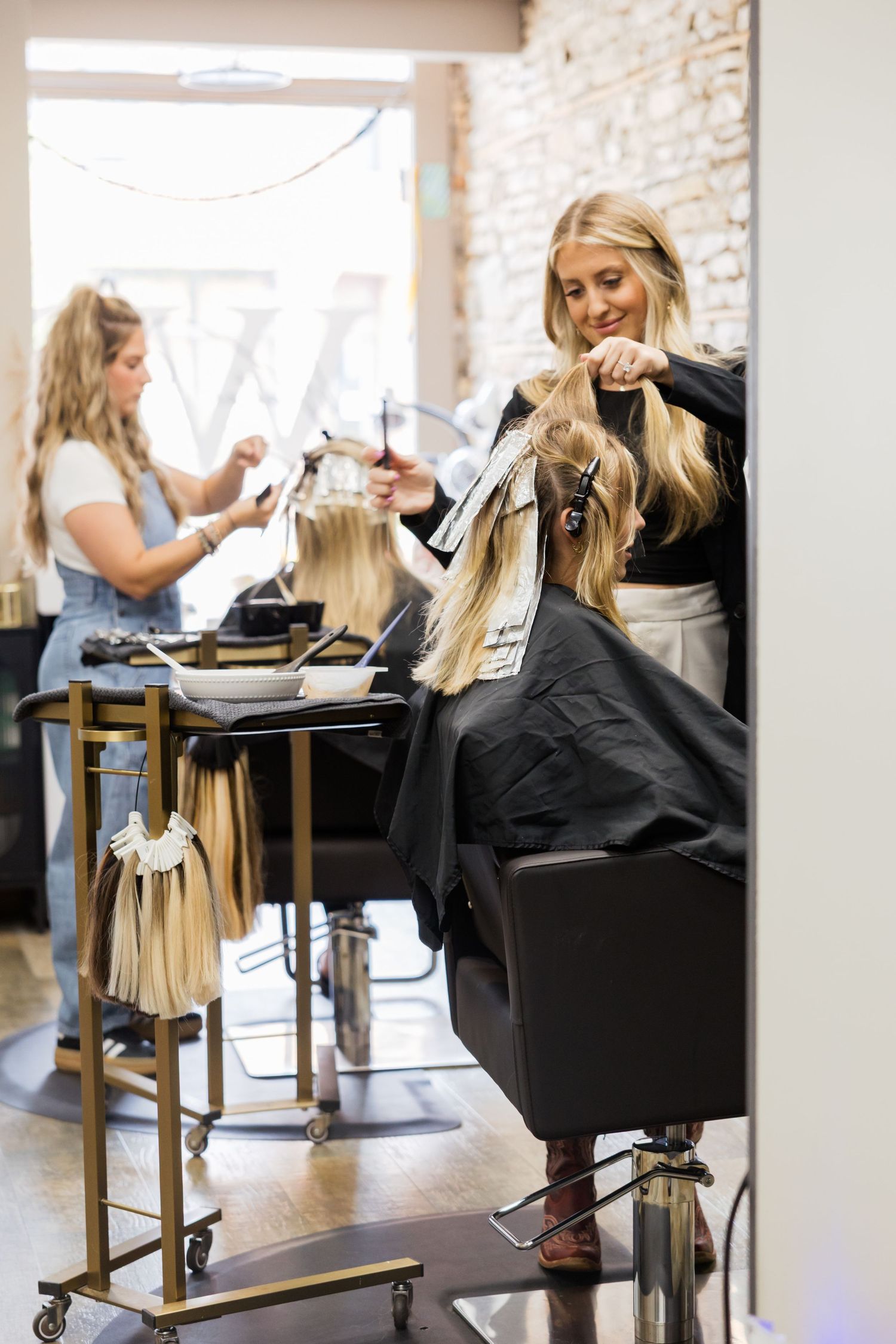 A sequence of salon styling chairs shows clients getting hair services at a modern brick-walled beauty salon.