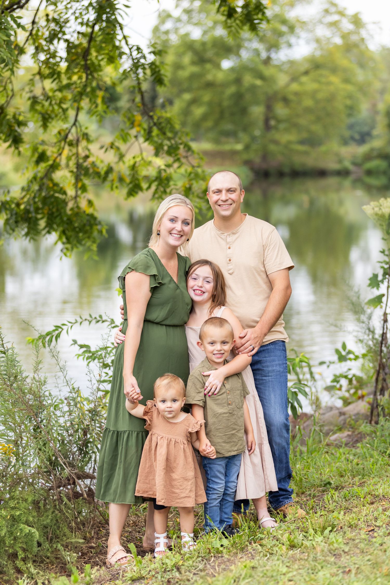 Family portrait by lakeside with green trees and water in background.