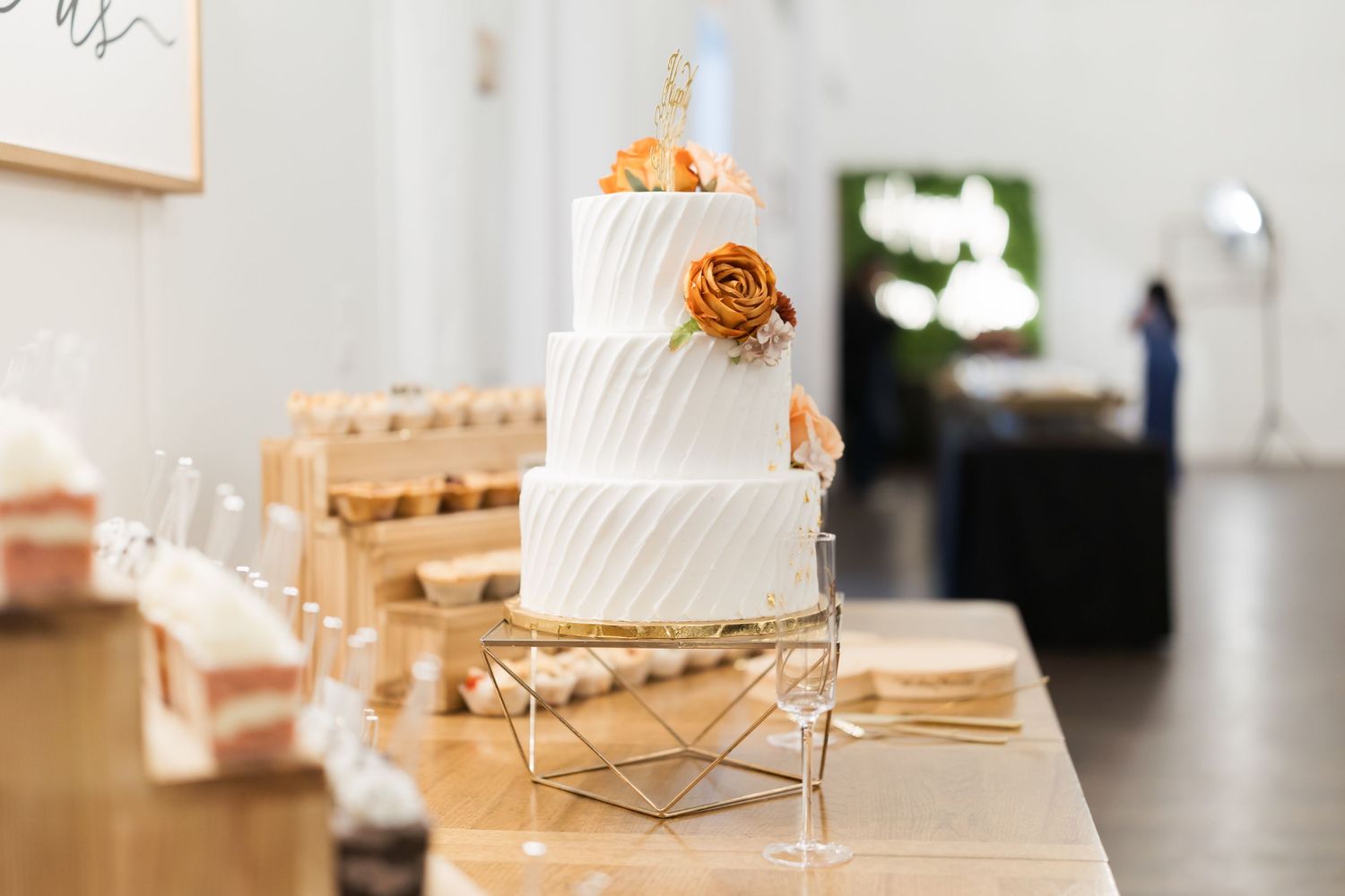 Elegant white wedding cakes displayed on gold stands against a light background.