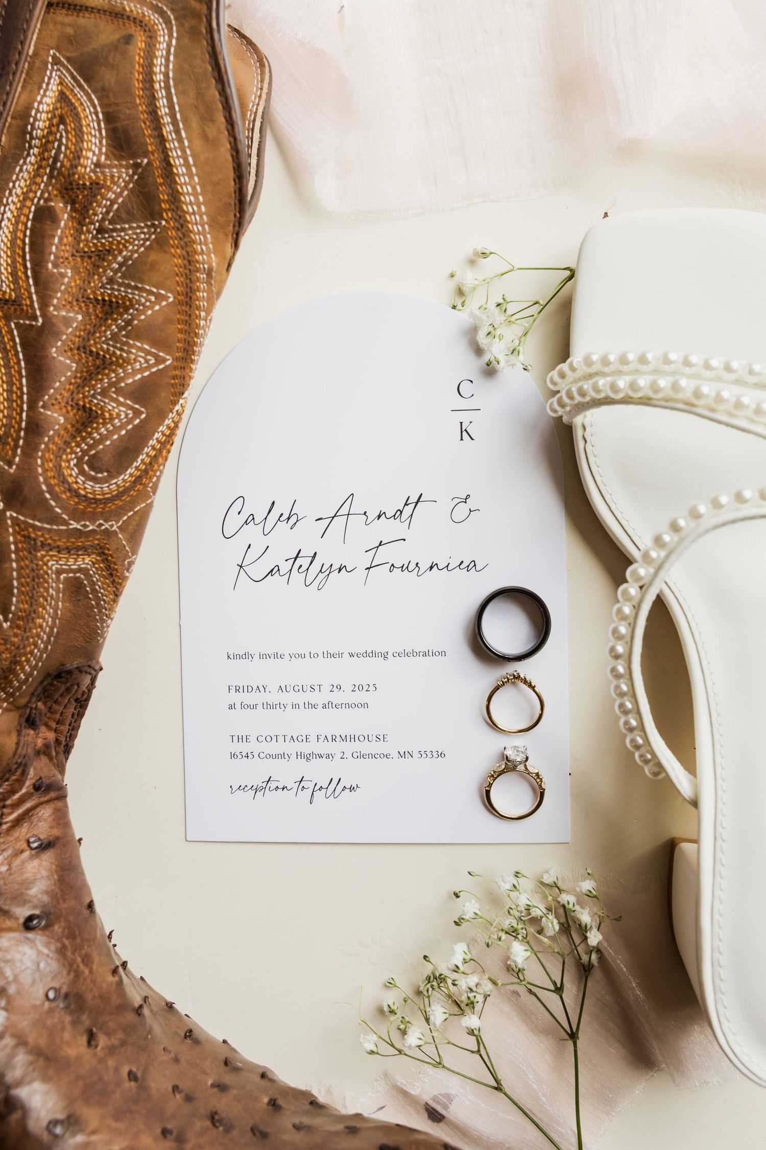 Wedding details including brown leather cowboy boots, wedding rings, and delicate invitation on cream background.