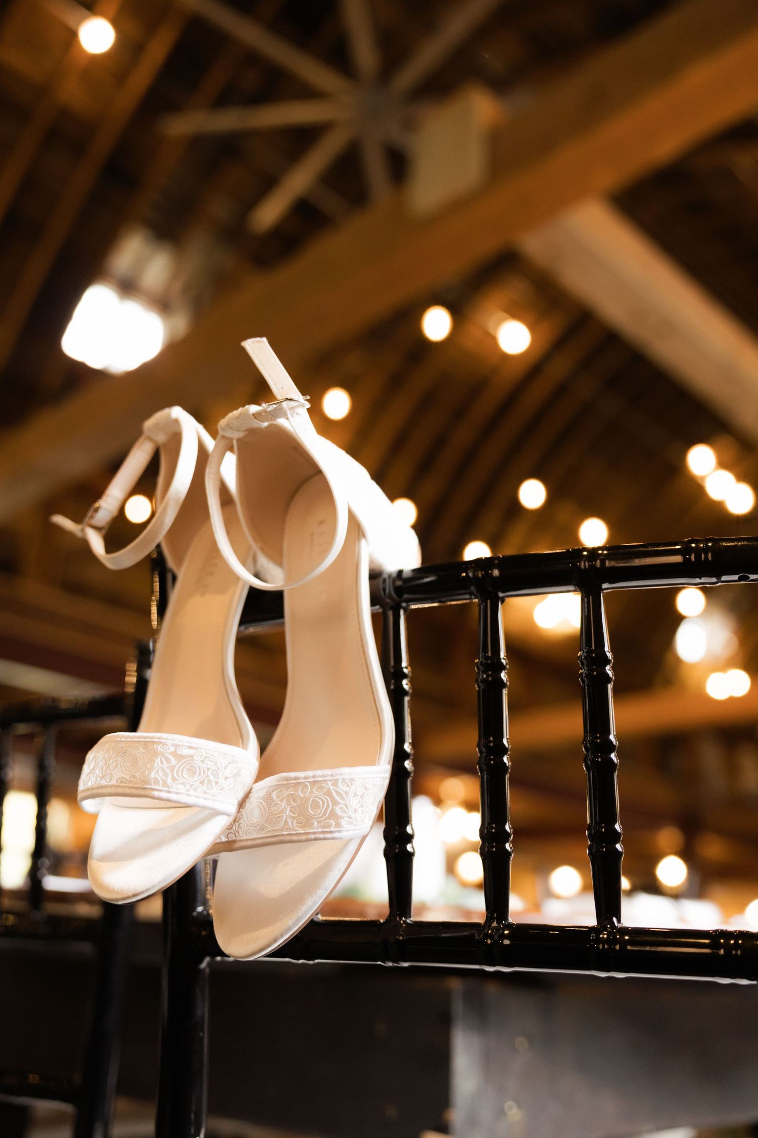 White bridal heels displayed on black railing with twinkle lights in background.