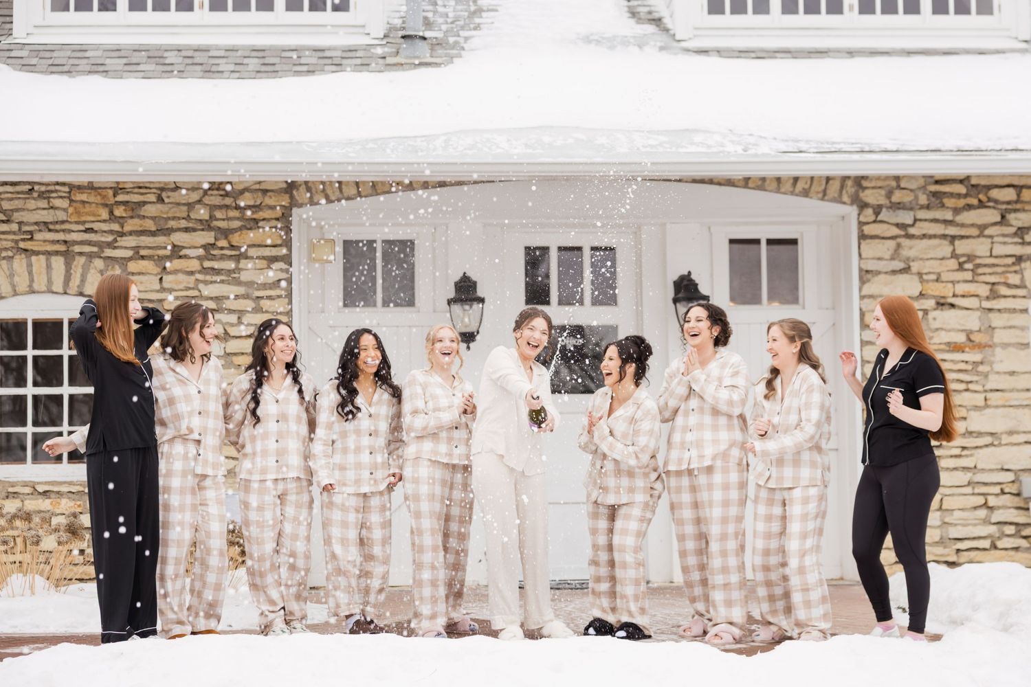 Wedding party posing in front of stone building during winter snowfall.
